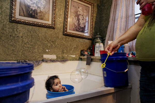 Agriculture is responsible for 95 percent of aquifer use and families at the fringes of the aquifer feel it. For four years now, approximately 30 families near Clovis, NM,  can no longer get water from their wells and carry water home need for cooking and bathing.  This two-year old has a bubble bath sharing precious water with a family of nine that requires 105 gallons a day.
County Road 5 is the canary in the coal mine for Ogallala depletion. Just across the state line from here are 88,000 wells in the Texas panhandle. Those wells use approximately 200 gallons a minute according to HPWD. When they started irrigating, the wells poured out 1000 gallons a minute. Portales is a medium size city that uses three agricultural wells to give city water to the entire town and purchasing land around the wells to protect the resource.
Across the amount of water used by agriculture at the Texas border is the equivalent of 10,000 towns the size of Portales. When those wells were in full production, it was more like 50,000 cities sucking water just over the state line. A home healthcare worker lives with her daughter and partner and nine other family members require 1over 100 gallons a day to meet their water needs. She hauls water to her home daily using 21 5-gallon blue plastic buckets that she loads into the back of a small pickup truck. A daughter quit her job and returned home to help to carry water when her mother had health issues and she became the primary water carrier.
When the water crisis hit County Road 5 the family thought it was temporary, and they would get a hotel room for the weekend to shower or go to a friends home. As it became obvious the water was never coming back, they quietly started hauling water. One local county commissioners heard about this family’s situation and was aghast at the third world narrative. The commissioner said now there are only 30 or so families in this dire situation and wonders what will happen if the numbers climb to 100 and it becomes public that they running out of water.  “I think everyone will just leave,” he says.
