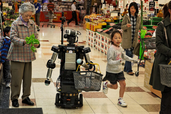 Shopping and Companion Robots and for Elderly | Kyoto, Japan
A talking robot helps 69-year-old Nabeshima Akiko shop in a test conducted by researchers from Keihanna Science City near Kyoto. Making up 23 percent of the population, the 29 million elderly in Japan far outnumber the young, an unprecedented situation that raises concerns about who—or what—will support the old in the years ahead.
The robotics folks at Keihanna Science City are developing robots to help the elderly with shopping and other chores, but mostly they are developing companions to combat kodo kushi (lonely death). The elderly Japanese person fills out a shopping list at home on their iPhone and when they walk into the store the robot recognizes them from the geolocation info in their iPhone and throws it arms in the air and says “you are here . . . and want to buy apples . . . we have some great new apples over here . . . come with me.” The robot accompanies the woman on her shopping tasks, carrying the basket and reminding her of the items on her list. The eyes of the robot follow her wherever she stands by paying attention to the iPhone geolocation data in order to give the elderly the impression they have a friend. 
