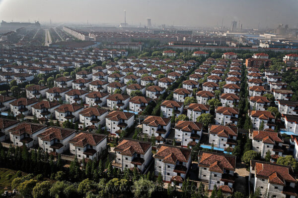 The largest urbanization in human history is from the Chinese countryside to the cities. It is predicted that 4.9 billion or 60 percent of humans worldwide will live in cities by 2030.
Huaxi Village (Farmer’s Village) is emblematic of the beginning of the massive urbanization of China and of the largest human migration in history from the rural areas of China into the cities. When I first visited China during the Tiananmen Square uprising it was difficult for people born in one city to move to another. If your identity papers said you belonged to Xian you had to stay in Xian even though you might want to move to one of Deng’s economic zones like Guangzhou to a have a higher paying job. We ran the checkpoints where they examined your identity papers during this time because the police did not have guns or radios. I remember police jumping up and down on their little daises in the middle of the road—literally hopping mad—but there was nothing they could do but be angry as we sped away. Not that many nationals had cars during that time, so they could stop them and check their identity papers and turn them away from a better life. When those checkpoints went away and there was free movement in China, 1.3 billion people finally had a chance to follow their dreams and moved to the cities. The Chinese mass migration into cities is a large part of why we are now an urban species. Fifty one percent of us live in urban areas throughout the world. 
In Huaxi Village they didn’t have to migrate, they changed their model rural farm into a modern industrial city. They started factories, but initially worked in them secretly (no windows). When government officials came around, all the workers ran out into the fields and pretended to be peasants. They became the first and most successful capitalist exploitation of the collective. There have been 30,000 official government visits to this place to see how it is run every year. There are not many model farms left in China, and none with this wealth. This model farm runs about 80 factories, including garment factories and steel mills. Huaxi Village is touted by the current government as the most successful transition from farm to modern industrial city.
