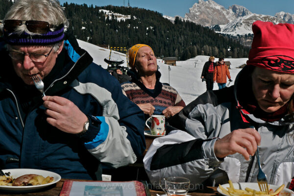 Skiers eat and sun at a restaurant in the Suiusi ski area of the Dolomites in northern Italy. Tourists ski around the mountains taking a series of lifts that connect miles of skiing, and then they take breaks to relax and enjoy the outdoors on a winter holiday.
The sunny Dolomites are made of a carbonate rock that is pale in color. Although technically in Italy, the locals speak German first, a result of a history that aligns them more with regions to the north.
