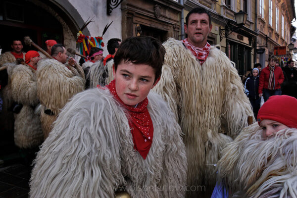 Carnival is celebrated in the Slovenian countryside displaying a variety of costumes and individual characters among which the most popular is the Kurent (plural: Kurenti), a monstrous and demon-like, but fluffy figure.
Costumes of long, white fur and large cowbells are very old traditions and the highlight of the Ptuj Carnival parade. A father and son remove their heavy, hot masks to take a break during the merry making.
The lore of Pust or Carnival in old Europe traces back to Pagan beliefs that the dark and cold winter was caused by evil.  When people found the first signs of spring, they celebrated when light won over the darkness of winter.
