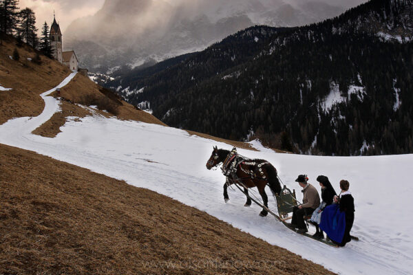 A horse drawn sleigh carries three members of the Ladin community of LaValle up the mountain to the church. Generations of families follow the traditions of their elders wearing simple costumes and speaking their unique Romache language.  Spring melts winter snows, but the skies remain gray in the rural region in the Dolomites of Italy.
Ladina is a region in north Italy where people live following traditions of an ancient culture that is unique to the Dolomites, and with roots dating as far back as the Roman Empire.
