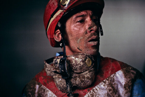 A mud-splattered face alludes to the hardships of a jockey’s life. Smeared goggles tossed aside from being in the back of the pack, Rene Douglas had just completed a race at Lexington’s Keeneland Race Course on a rainy race day. A jockeys life is not easy—this elite club of professional athletes maintain a near inhuman weight restriction that most Americans would never even attempt.
Jockeys face unpredicted dangers riding a 1,000-pound animal at high speeds competing for a win. Racing injuries often mean costly and uninsured medical expenses, the end of a career, or worse. Still, horse racing lures die-hard talent. “I’ve got three herniated discs in the neck,” says Rene Douglas. “I love the sport because I ride good horses and I’m good at it.”  Douglas endured injuries to his spinal cord from an unfortunate accident in a race that his mount did not survive. He is paralyzed from the waist down.
 
