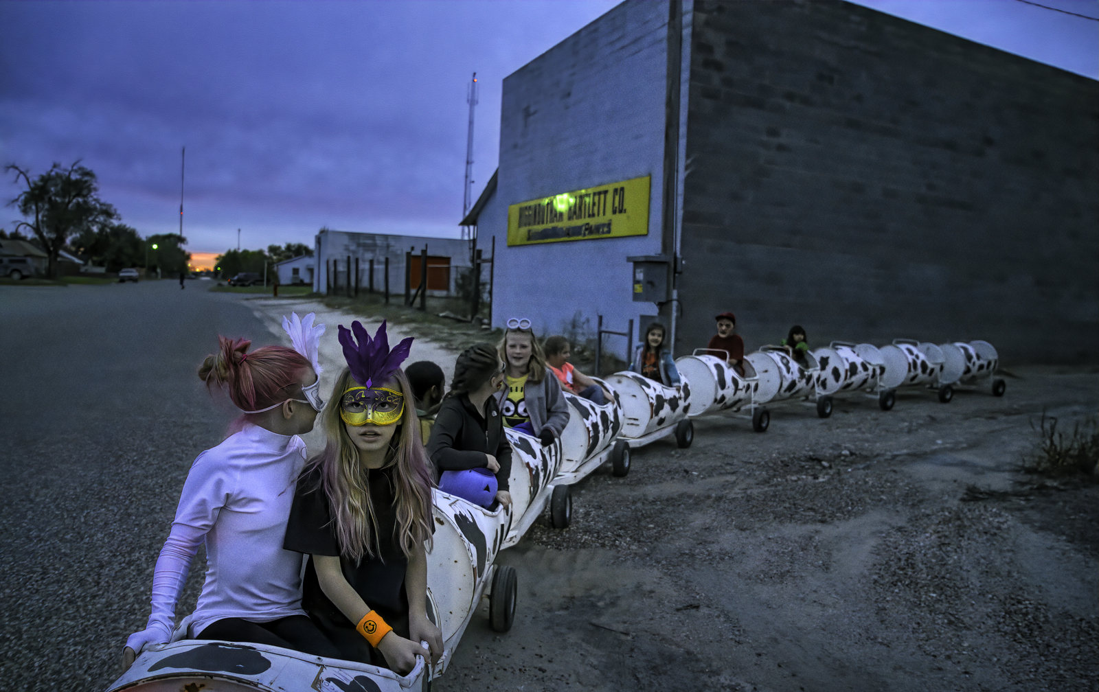 Costumed children ride in train of large drums in blue light creating a surreal scene