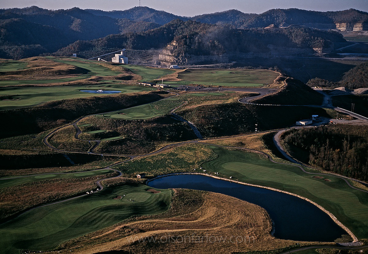Birds-eye view onto scenic golf course with working mine in background.