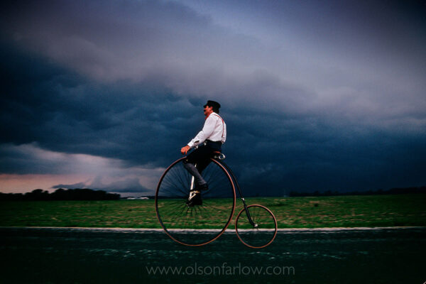 


A bicycle enthusiast dresses in clothes of the the 19th century era as he pedals ahead of an Indiana thunderstorm. When the road fell into decline, bicyclists banded together and The League of American Wheelmen was formed in 1880. They demanded potholes to be filled which began a revival of the National Road Construction began in Cumberland, MD in 1811 on the National Road, America’s first highway built with federal funds. Reaching Wheeling, West Virginia in 1818, it ended more than 600 miles west in Vandalia, Illinois in 1852. What began as a wagon train road to settle the West is now Main Street to many towns. Communities sprang up through Ohio, Indiana and IL during the beginning of a prosperous automobile era. As the railroad developed, the road’s importance diminished. Bypassed later by the Interstate, many towns began to decline. The road today is a tapestry of different eras–old stone taverns and a few historic remnants from early years.



