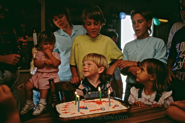Candles are lit on a cake and family surrounds four-year-old Jake while singing “Happy Birthday” during a party in rural Florida.
