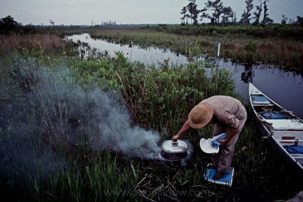 Cooking dinner involves creative thinking on a wilderness canoe trip through the Okefenokee Swamp. This outdoorsman stands on seat cushions taken from his boat to keep his feet dry while boiling potatoes over a campfire.
The Okefenokee Swamp is a deep bog of thick peat moss and fresh “blackwater” that is home to 440 species of birds, mammals, and reptiles, many of which are endangered. The 402,000-acre wetlands was designated a national wildlife refuge in 1937.

