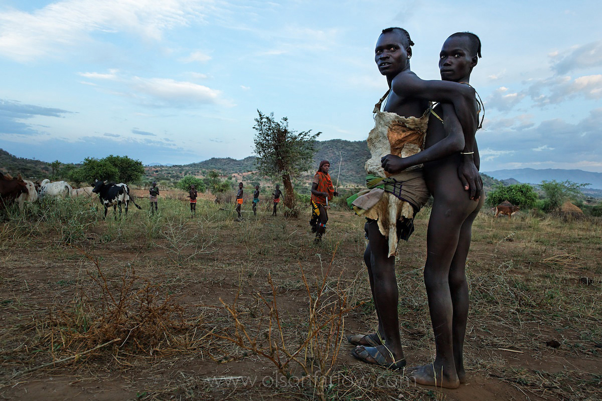 Two men standing in an open field, one is naked