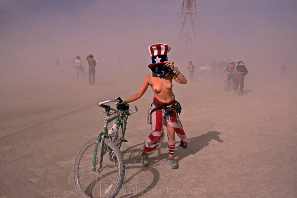 A sandstorm blasts across the desert of the Black Rock Playa in northwest Nevada.
Costumed and costumed revelers are vulnerable to the harsh conditions and changing environment of the salt flats during the annual Burning Man Festival.
A semi-nude Uncle Sam struggles to keep her hat and bicycle from blowing away in a dust storm. As many as 50,000 people form a small city for one week reveling in the outdoors making art in the wilderness landscape.
 
