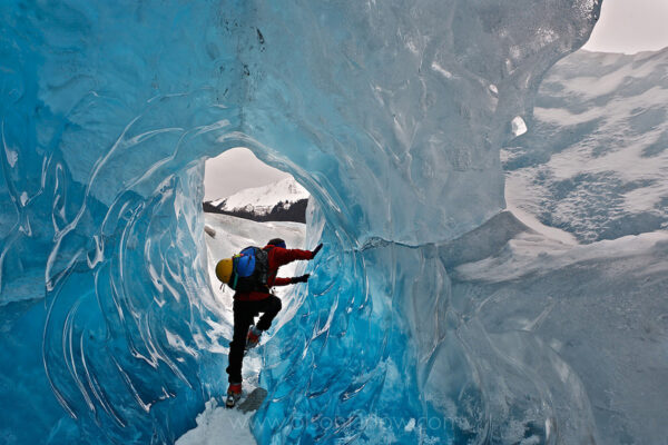 Equiped with crampons and emergency equipment, a hiker crawls through an ice tunnel formed in the Mendenhall Glacier. As the glaciers in southeast Alaska melt, ice is exposed thousands of years after being buried. Some tunnels in the 1,500-square-mile Juneau Icefield are connected to ice caves, which formed as the glacier moved across uneven surfaces.
During the Pleistoncene Great Ice Age several climate fluctuations created glacial advance and retreat, and vast sheets of ice covered nearly a third of the Earth’s land mass and one half of Alaska.
As the climate warmed during the Holocene, ice retreated remaining in Alaskan at high elevations. The most recent variation in advance and retreat created the Juneau Icefield formed 3,000 years ago and ending in the 1700’s. Mendenhall Glacier has flowed for 250 years for 13 miles ending in a lake at its’ base.
