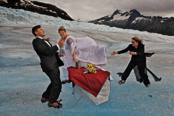 Tourists are drawn to the beauty of Alaska and its glaciers, some for the ultimate and most unlikely experience—donning crampons for their wedding on ice.
If the weather cooperates, couples can arrange for a limousine from a cruise ship to the airport for a helicopter ride onto a glacier for a traditional ceremony with tuxedo and white wedding dress and extra touches including wedding cake, music, and flowers.
The groom pops the cork on a bottle of champagne provided by Diane Pearson, who married this couple on the Mendenhall Glacier near Juneau.

