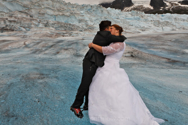 Wedding kiss begins the celebration at a marriage on top of “God’s cathedral.”  The Mendenhall Glacier in the Tongass National Forest was a perfect setting for the couple who met on the Internet, and decided to be married in an unusual way.
The weddings are arranged so that if the weather is good, a couple straps on crampons and a helicopter whisks them off to the Juneau icefield. They are picked up again after their exchange of vows and a reception party that includes a cake, flowers and music.
